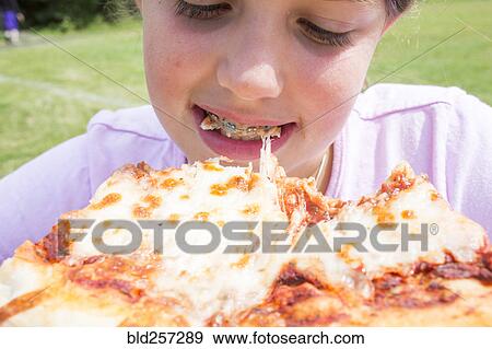 Stock Photo - Close up of Caucasian girl with braces biting pizza. Fotosearch