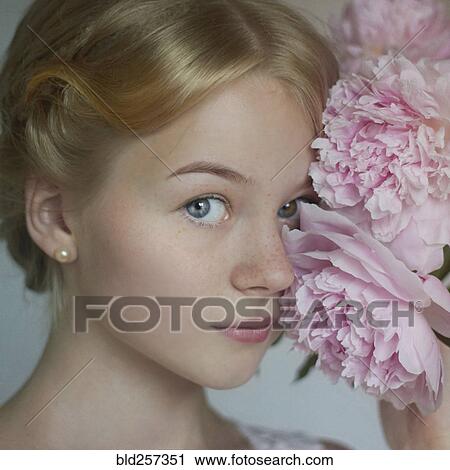 Stock Image - Close up of Caucasian teenage girl holding flowers to face. Fotosearch