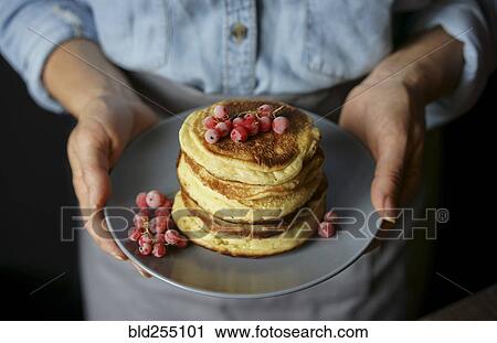 Stock Image - Close up of Caucasian woman holding plate of pancakes. Fotosearch