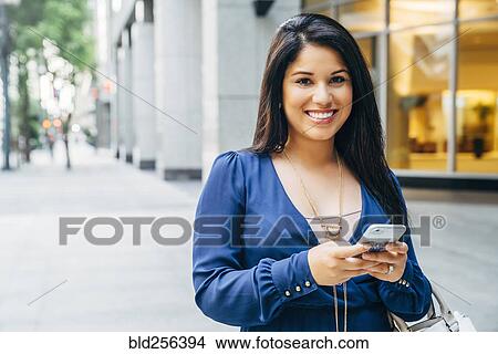 Picture - Close up of Hispanic woman texting on cell phone in city. Fotosearch