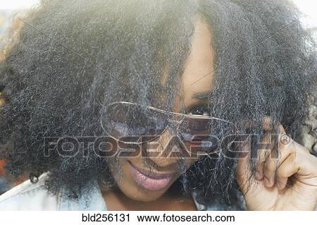 Stock Image - Close up of mixed race woman peering over sunglasses. Fotosearch