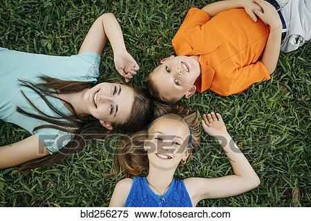 Stock Photography - Close up portrait of smiling Caucasian brother and sisters laying on grass. Fotosearch