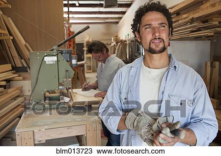 Stock Image - Co-workers woodworking in workshop. Fotosearch