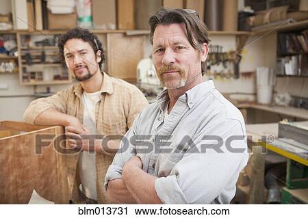 Stock Image - Co-workers woodworking in workshop. Fotosearch