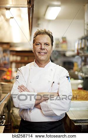 Picture - Confident Caucasian chef standing in commercial kitchen. Fotosearch