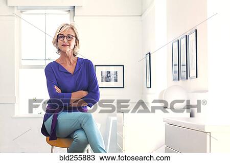 Stock Image - Confident Caucasian woman sitting on stool. Fotosearch