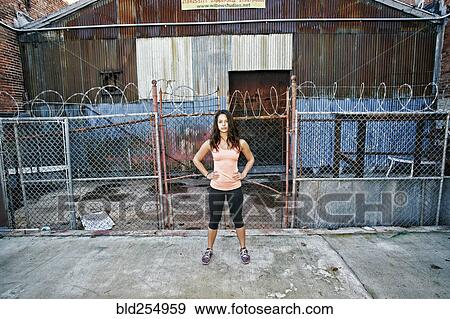 Stock Photo - Confident mixed race woman standing on sidewalk near barbed-wire fence. Fotosearch