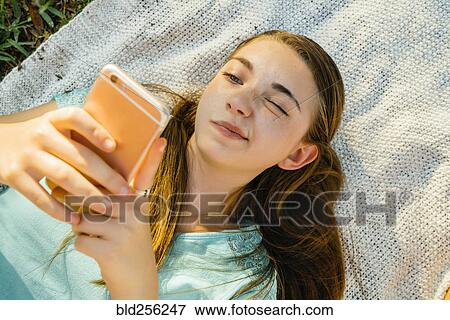 Stock Photo - Confused Caucasian girl laying on blanket texting on cell phone. Fotosearch