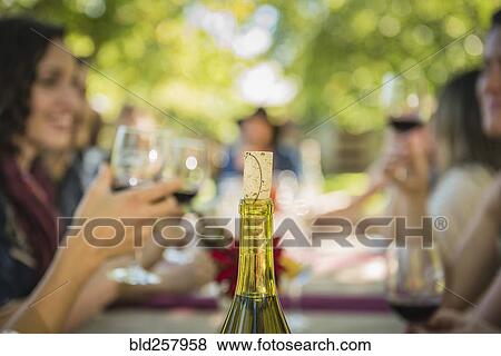 Stock Photo - Cork in wine bottle near people drinking wine. Fotosearch