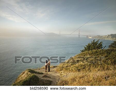 Stock Image - Couple admiring scenic view of bay. Fotosearch