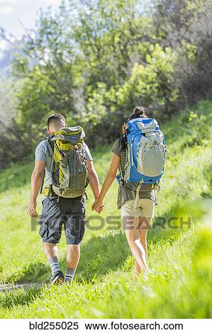 Stock Photography - Couple carrying backpacks hiking on hill. Fotosearch