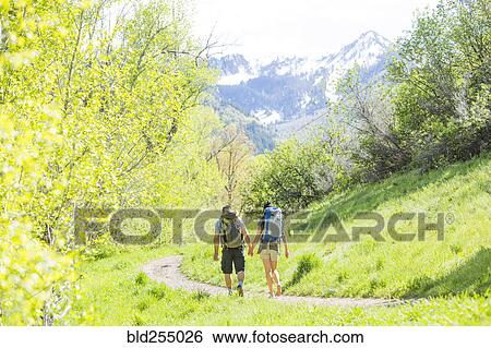 Stock Photograph - Couple carrying backpacks hiking on path. Fotosearch