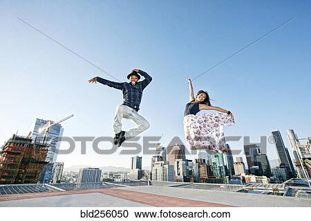 Stock Image - Couple dancing and jumping on urban rooftop. Fotosearch