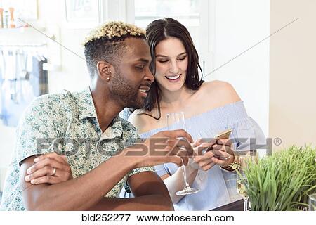 Stock Photo - Couple drinking champagne and texting on cell phone. Fotosearch