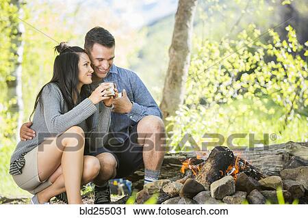 Stock Image - Couple drinking coffee near campfire. Fotosearch