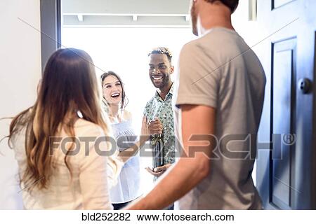 Couple greeting friends bringing wine bottle at door View Large Photo Image Stock Image - Couple greeting friends bringing wine bottle at door. Fotosearch