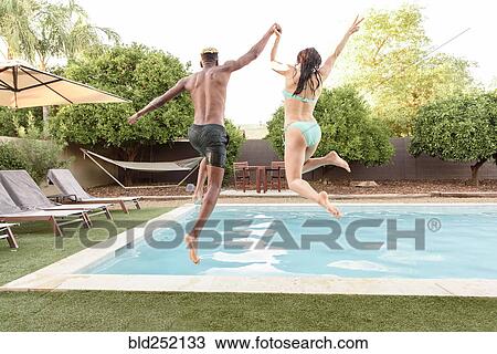 Couple holding hands jumping into swimming pool View Large Photo Image Stock Image - Couple holding hands jumping into swimming pool. Fotosearch