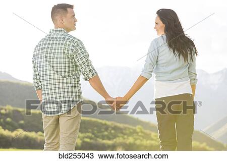 Stock Image - Couple holding hands standing near mountain. Fotosearch
