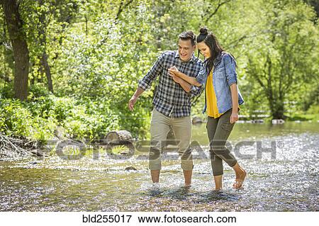 Stock Photo - Couple holding hands wading in river. Fotosearch
