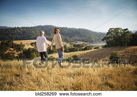 Stock Photo - Couple holding hands walking in field. Fotosearch
