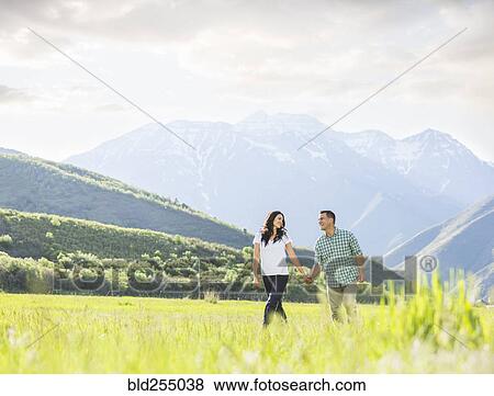 Stock Photo - Couple holding hands walking near mountain. Fotosearch