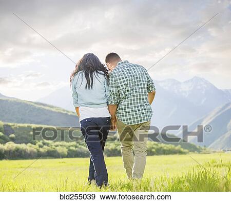 Stock Photo - Couple holding hands walking near mountain. Fotosearch