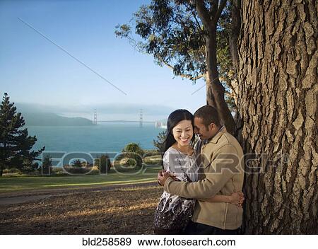 Stock Photo - Couple hugging at tree near bay. Fotosearch