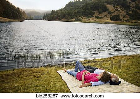 Stock Photo - Couple laying on blanket near lake. Fotosearch
