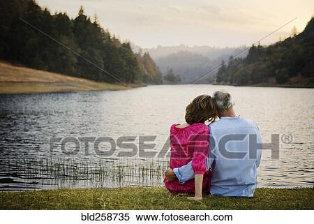 Stock Photography - Couple sitting in grass and hugging near river. Fotosearch
