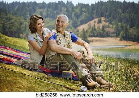 Stock Photo - Couple sitting on blanket near lake with fishing rod. Fotosearch