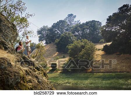 Stock Photo - Couple standing on rocks admiring river. Fotosearch