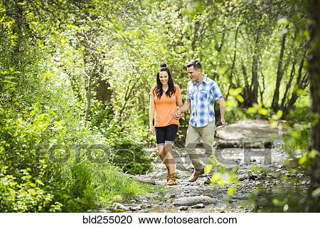 Stock Image - Couple walking in the woods holding hands. Fotosearch