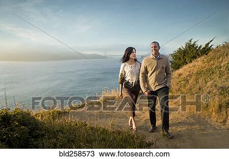 Stock Image - Couple walking on path near bay. Fotosearch