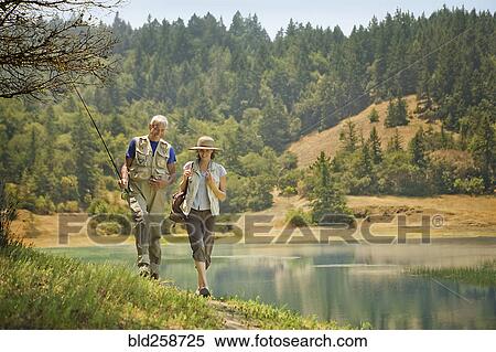 Stock Photography - Couple walking with fishing rod near river. Fotosearch