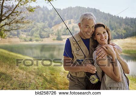 Stock Photograph - Couple with fishing rod hugging near river. Fotosearch