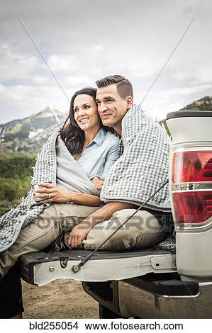Couple wrapped in blanket sitting on bed of pick-up truck View Large Photo Image Picture - Couple wrapped in blanket sitting on bed of pick-up truck. Fotosearch