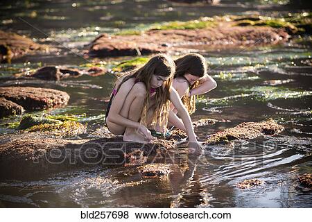 Stock Photo - Crouching Caucasian girls exploring tide pools. Fotosearch
