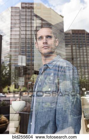Curious Caucasian man drinking coffee near window in city View Large Photo Image Picture - Curious Caucasian man drinking coffee near window in city. Fotosearch