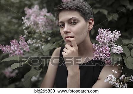 Stock Image - Curious Caucasian woman near flowering tree with finger on lip. Fotosearch