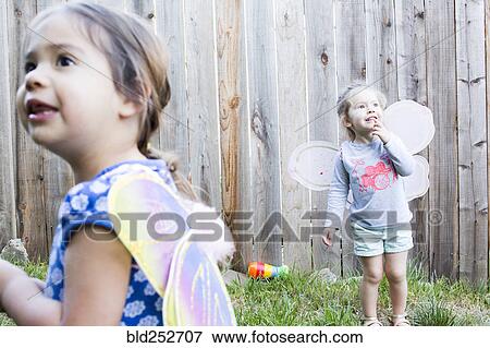 Stock Photo - Curious girls wearing fairy wings in backyard. Fotosearch