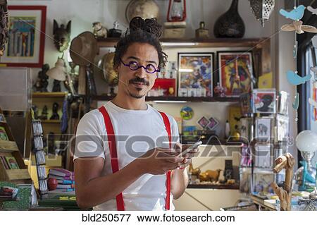 Stock Photo - Curious mixed race man wearing suspenders texting on cell phone. Fotosearch