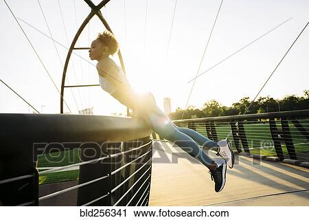 Stock Image - Curious mixed race woman leaning on bridge railing. Fotosearch