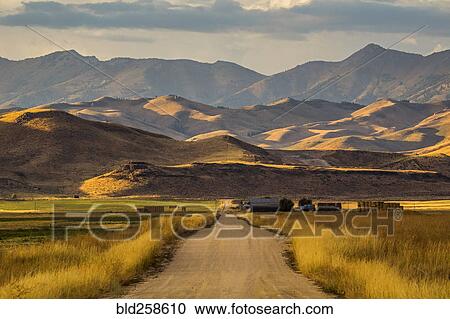 Stock Image - Dirt road to farm and mountains. Fotosearch