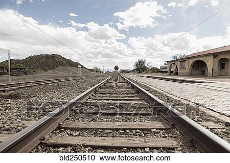 Distant Caucasian boy walking on train track View Large Photo Image Stock Image - Distant Caucasian boy walking on train track. Fotosearch