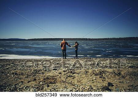 Stock Photo - Distant Caucasian couple holding hands on beach. Fotosearch