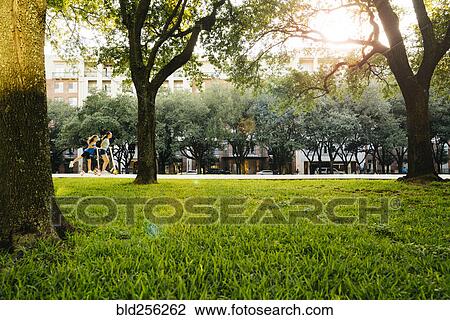 Stock Image - Distant Caucasian girls riding scooter in park. Fotosearch
