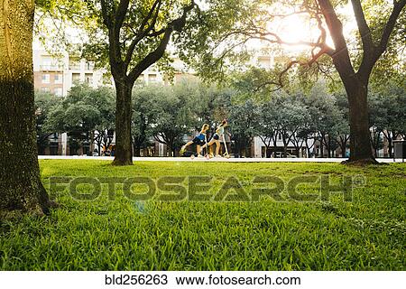 Distant Caucasian girls riding scooter in park View Large Photo Image Stock Image - Distant Caucasian girls riding scooter in park. Fotosearch