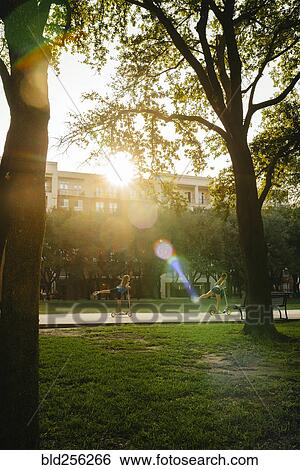 Stock Photograph - Distant Caucasian girls riding scooter in park. Fotosearch