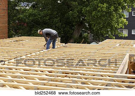 Stock Photo - Distant Caucasian man hammering frame at construction site. Fotosearch
