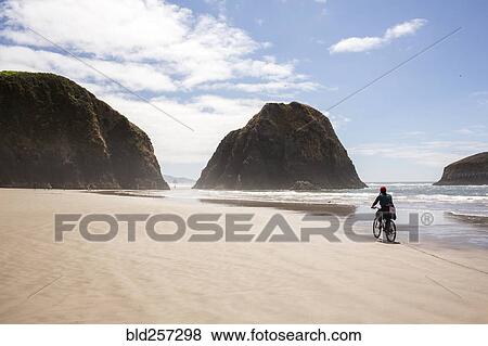Stock Photo - Distant Caucasian woman riding bicycle on beach. Fotosearch